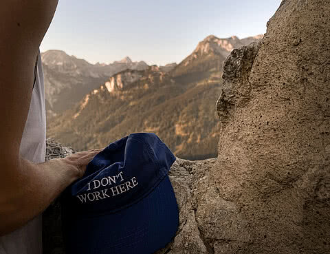 Blaue Kappe mit Aufschrift „I don’t work here“ an einem Fenster der Burgruine Falkenstein mit Blick auf die Allgäuer Berge
