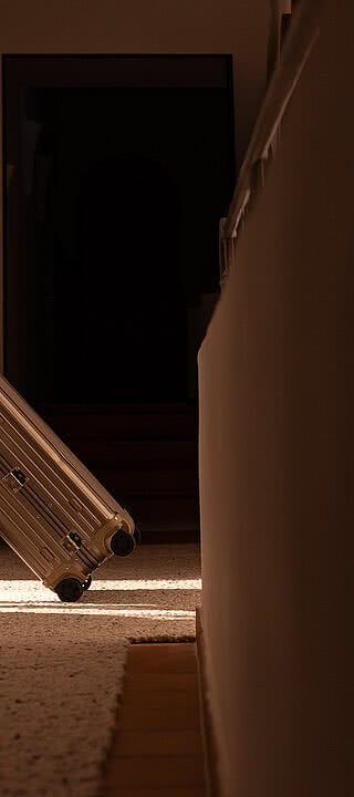 Der silberne Rimowa-Koffer wird im hellen Flur mit Steinmauer und Teppichboden, des Boutique-Hotels Blaue Burg bewegt.