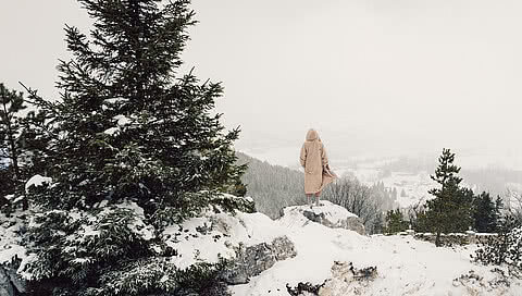 Person im Bademantel steht auf einem Felsen am Falkenstein im Winter